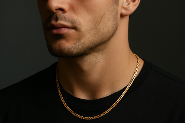 Professional product photograph of a delicate gold curb chain necklace on a young man from the front