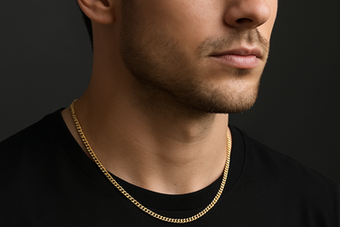 Professional product photograph of a delicate gold curb chain necklace on a young man